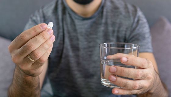 Mann, hält ein Glas Wasser und eine Tablette in der Hand.