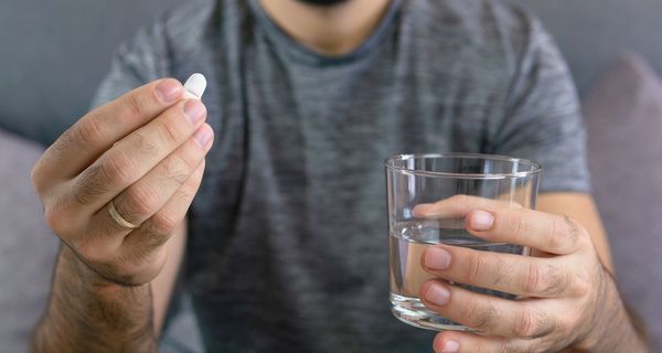 Mann, hält ein Glas Wasser und eine Tablette in der Hand.