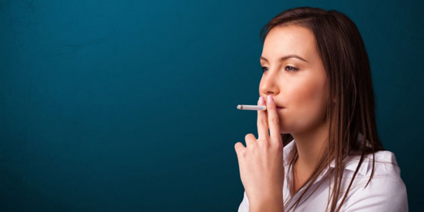 Junge Raucherin vor blauem Hintergrund zieht an einer Zigarette
