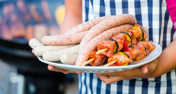 Kopflose Grillmeisterin mit Teller voll mit rohen Fleischspießen und Würsten