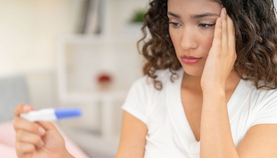 Eine Frau blickt besorgt auf einen Schwangerschaftstest, sein Ergebnis ist nicht zu erkennen.