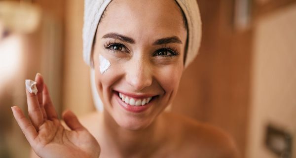 Junge Frau, Haare zu einem Handtuch-Turban gebunden, cremt sich das Gesicht ein.