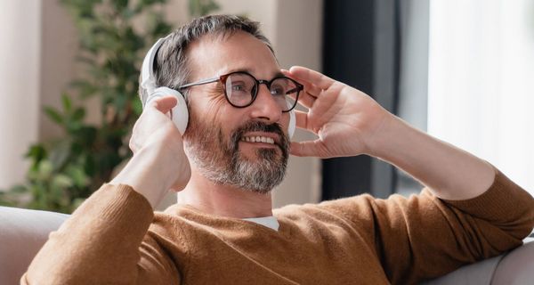 Mann sitzt zufrieden lächelnd auf dem Sofa und fasst sich an seine Kopfhörer.