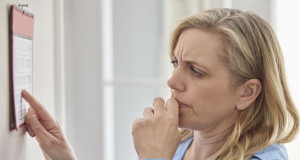 Eine Frau steht vor einem Kalender und blickt zweifelnd.