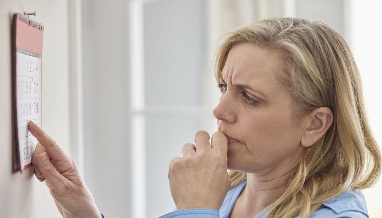 Eine Frau steht vor einem Kalender und blickt zweifelnd.