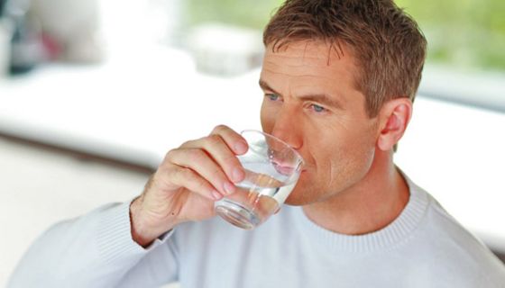 Mann mittleren Alters trinkt aus einem Wasserglas.