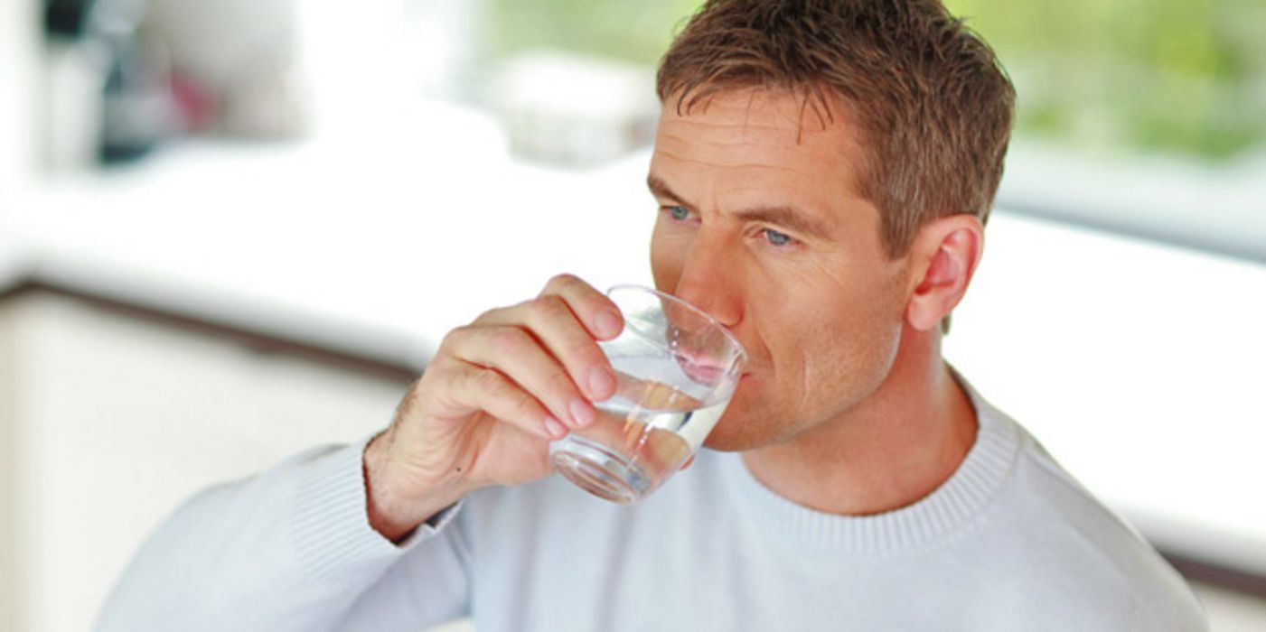 Mann mittleren Alters trinkt aus einem Wasserglas.