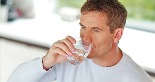 Mann mittleren Alters trinkt aus einem Wasserglas.