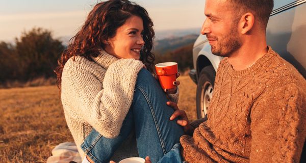 Paar, sitzt im Herbst draußen und trinkt Kaffee auf einer Wiese.