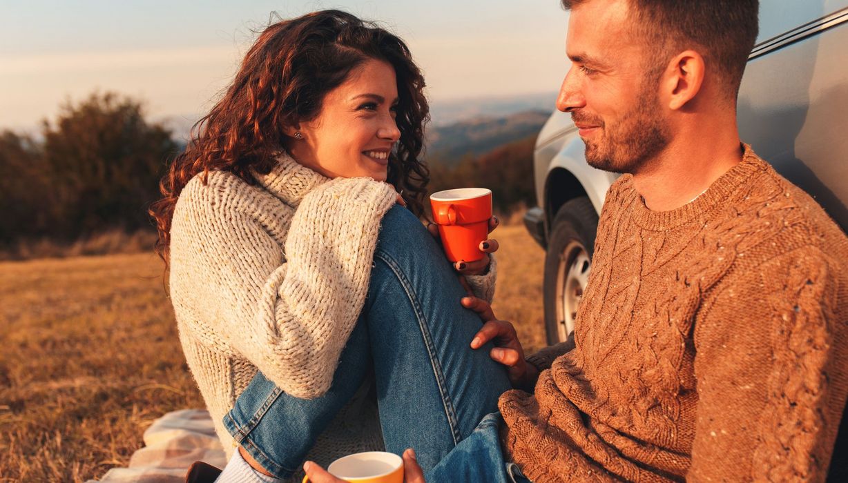 Paar, sitzt im Herbst draußen und trinkt Kaffee auf einer Wiese.