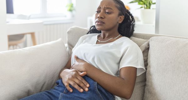 Junge Frau, liegt mit Bauchschmerzen auf dem Sofa.