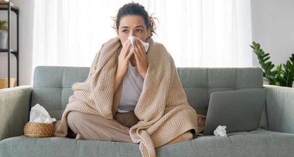 Junge Frau sitzt auf einem Sofa und putzt sich die Nase.