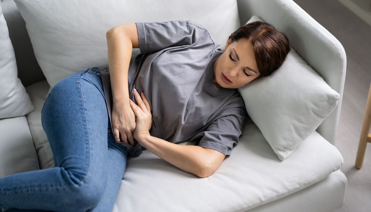 Frau liegt auf dem Sofa und hält sich den Bauch.