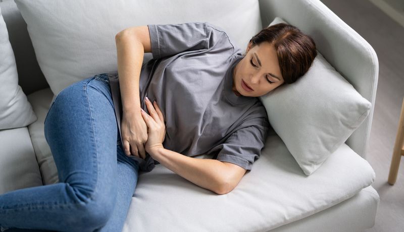 Frau liegt auf dem Sofa und hält sich den Bauch.
