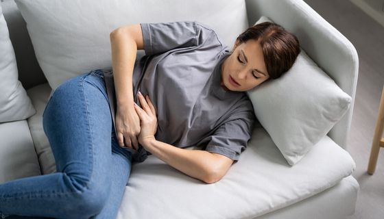 Frau liegt auf dem Sofa und hält sich den Bauch.