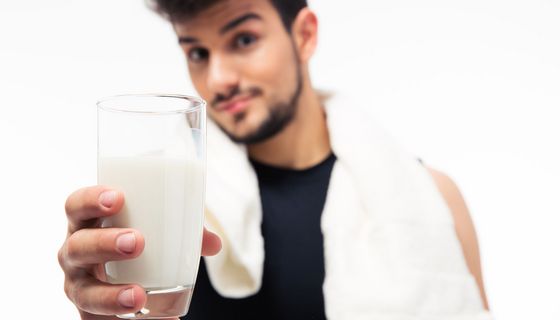 Junger Mann hält Glas mit Milch in die Kamera.