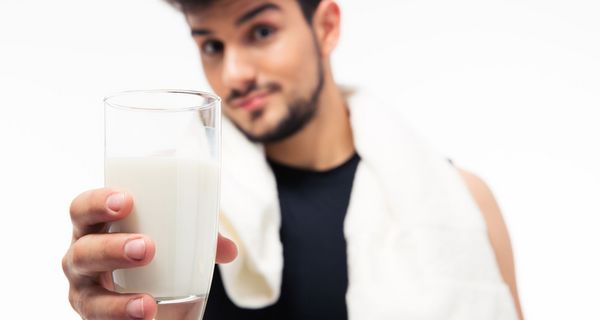 Junger Mann hält Glas mit Milch in die Kamera.