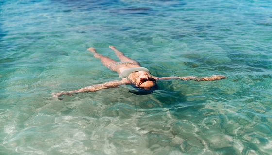 Frau, liegt im Meer rauf dem Rücken und lässt sich treiben.