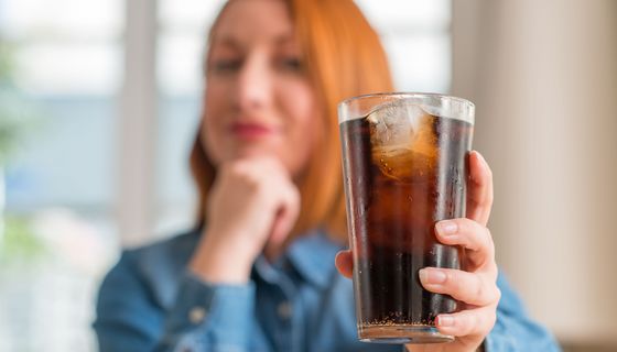 Eine Frau hält ein Glas Cola in die Kamera.