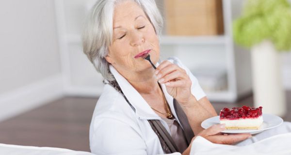 Ältere grauhaarige Frau isst genussvoll ein Stück Obsttorte