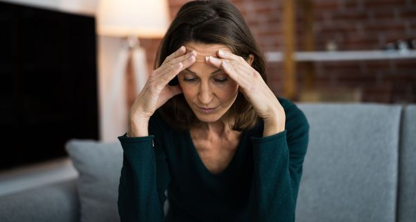 Frau, ca. 55 Jahre alt, hält die Hände an ihren Kopf und schaut zu Boden.