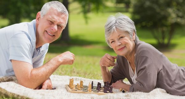 Älteres Paar liegt aus einer Picknickdecke und spielt Schach.