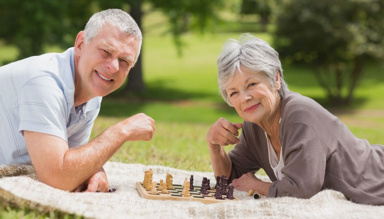 Älteres Paar liegt aus einer Picknickdecke und spielt Schach.