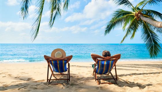 Mann und Frau im Liegestuhl unter Palmen mit Blick aufs Meer