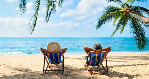 Mann und Frau im Liegestuhl unter Palmen mit Blick aufs Meer