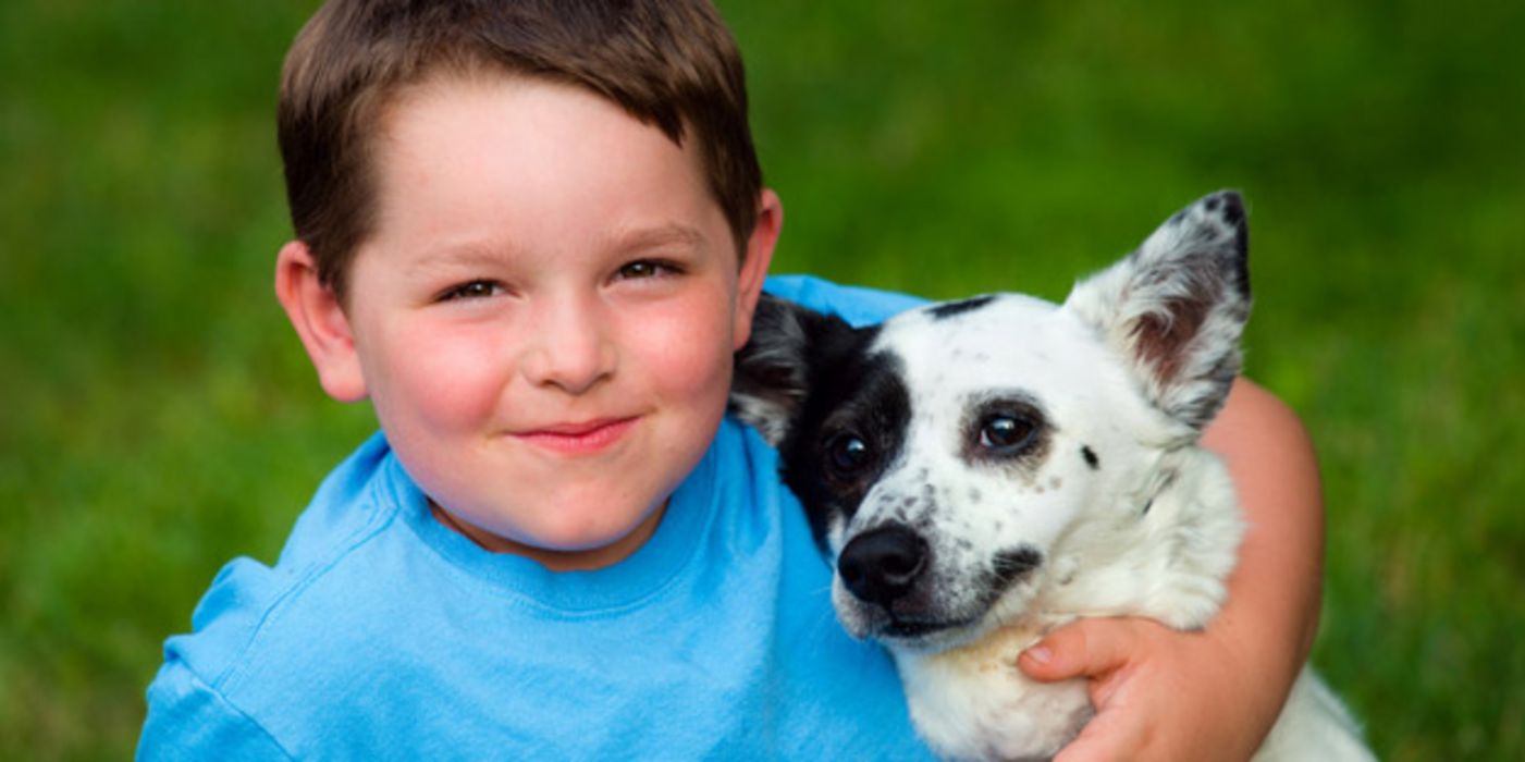 Junge mit blauem T-shirt mit kleinem Hund im Arm