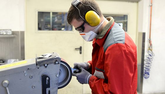 Profilfoto: Arbeiter, roter Overall, Mund-, Augen-, und Gehörschutz an Maschine