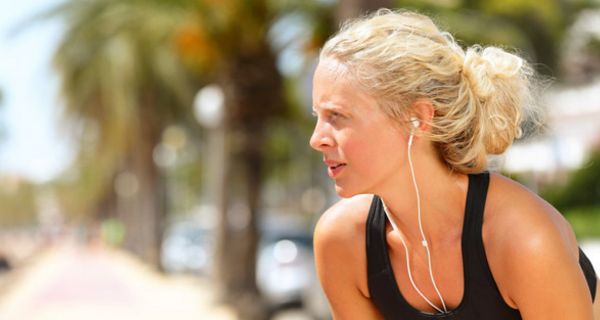 Junge blonde Frau mit Kopfhörern an einem heißen Sommertag, macht eine Pause vom Joggen.