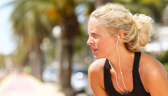 Junge blonde Frau mit Kopfhörern an einem heißen Sommertag, macht eine Pause vom Joggen.