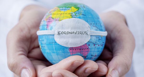 Hände, halten eine Weltkugel mit einem Coronavirus-Banner.
