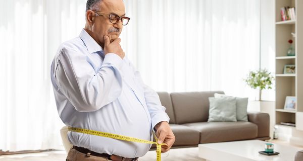Ein Mann über 50 misst seinen Bauchumfang.