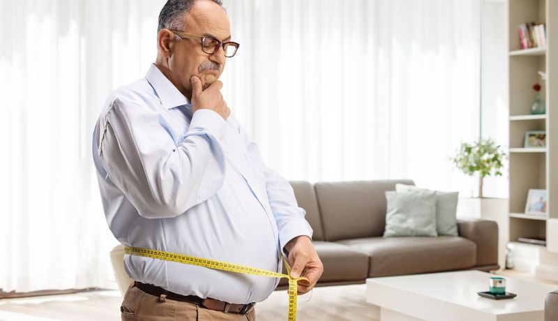 Ein Mann über 50 misst seinen Bauchumfang.