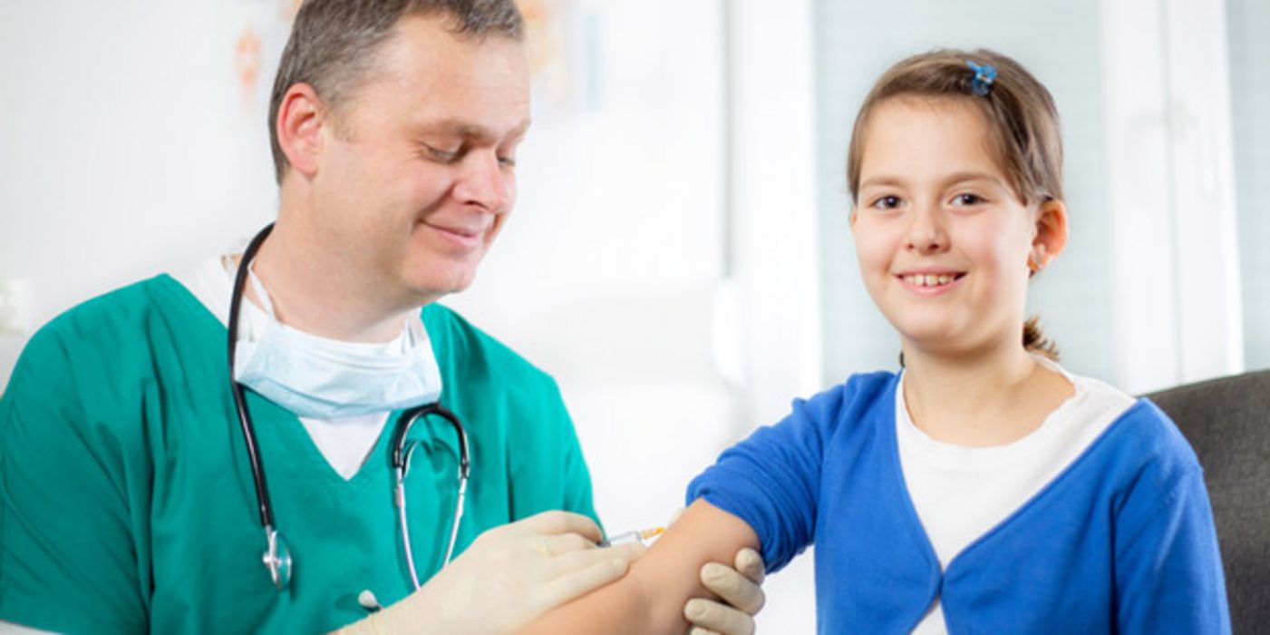 Mädchen, ca. 11 Jahre alt, wird von freundlichem Arzt in den rechten Arm geimpft. Beide lächeln.
