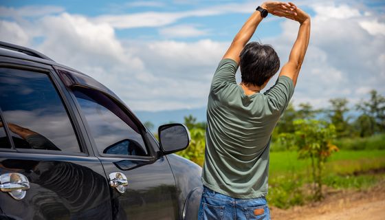 Mann steht neben dem Auto mit dem Rücken zur Kamera und streckt sich.