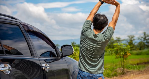 Mann steht neben dem Auto mit dem Rücken zur Kamera und streckt sich.