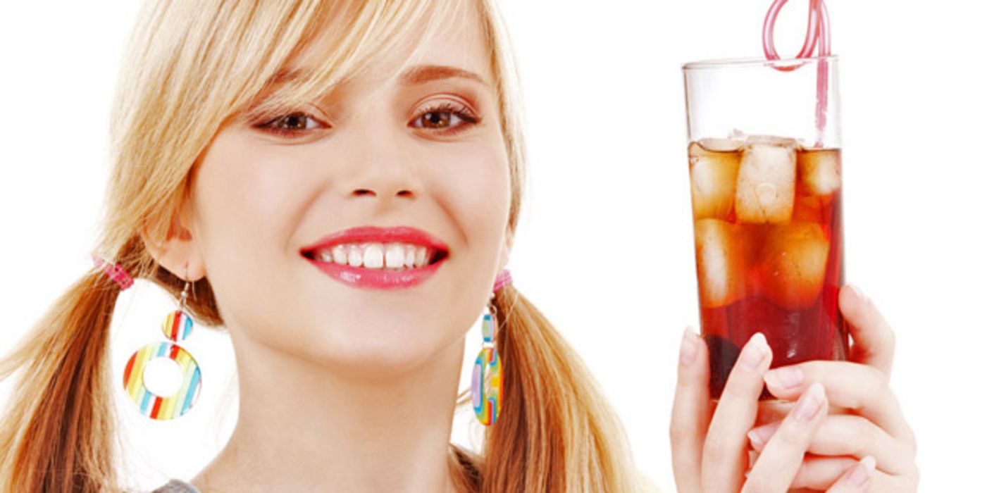 Blonde junge Frau hält ein Cola-Mixgetränk mit Eiswürfeln in den Händen