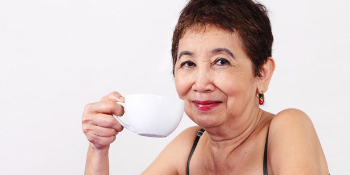 Frau um die 50 mit kurzen dunklen Haaren hält eine Tasse Kaffee in der Hand