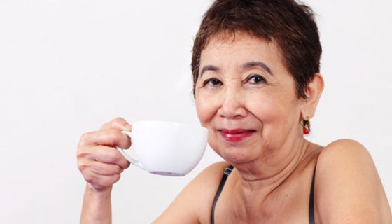 Frau um die 50 mit kurzen dunklen Haaren hält eine Tasse Kaffee in der Hand
