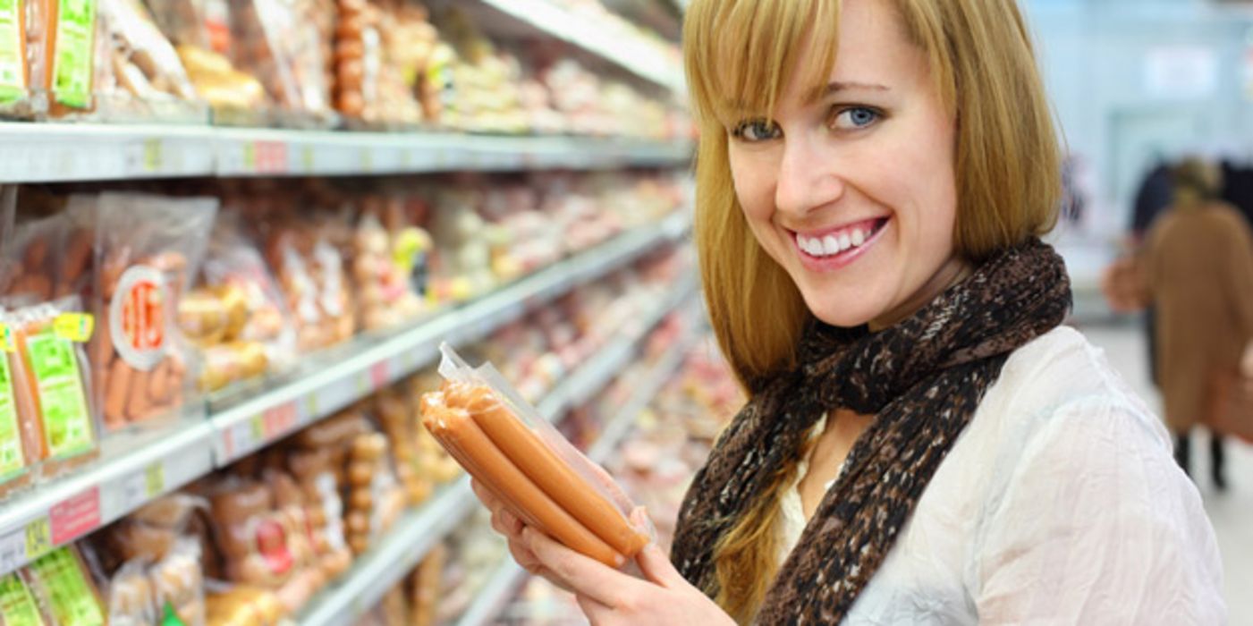 Frau im Supermarkt mit Würstchen in der Hand.