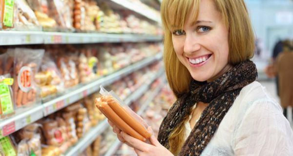 Frau im Supermarkt mit Würstchen in der Hand.