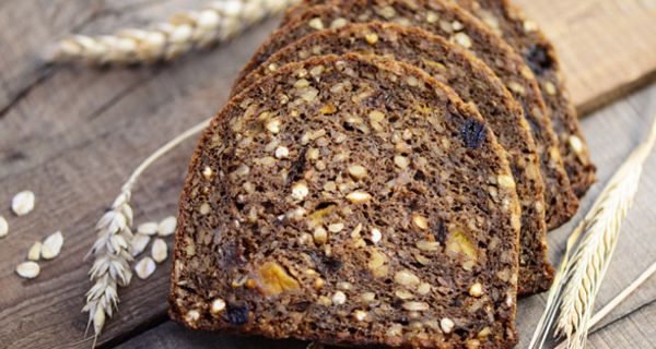 6 Scheiben Vollkornbrot auf Holztisch, einige Ähren als Deko