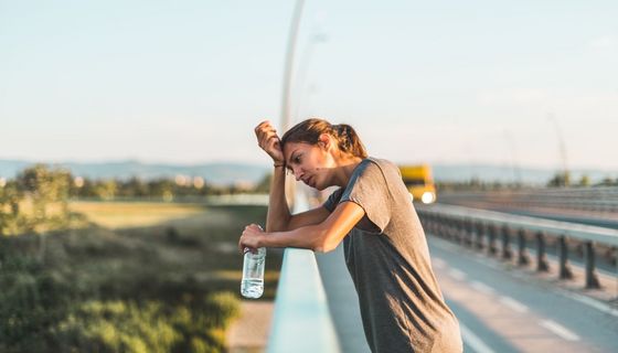 Frau in der Sommerhitze, lehnt an ein Geländer und trinkt Wasser.