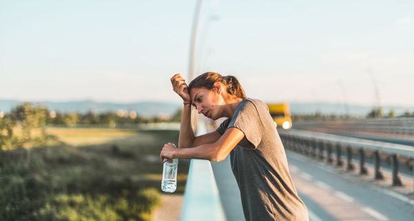 Frau in der Sommerhitze, lehnt an ein Geländer und trinkt Wasser.