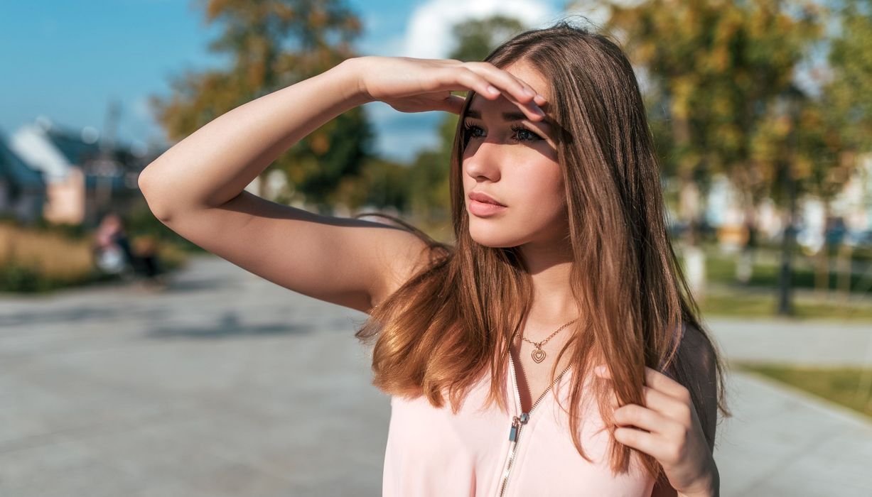 Junge Frau, hält eine Hand über ihre Augen, um sich vor der Sonne zu schützen.