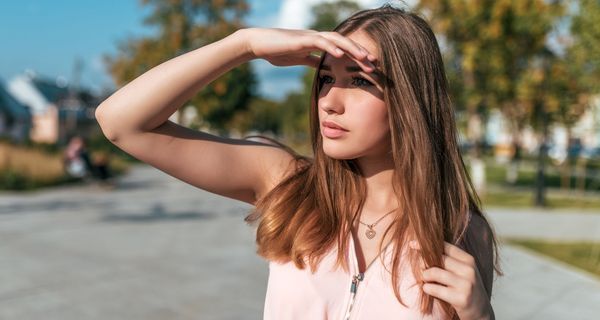 Junge Frau, hält eine Hand über ihre Augen, um sich vor der Sonne zu schützen.