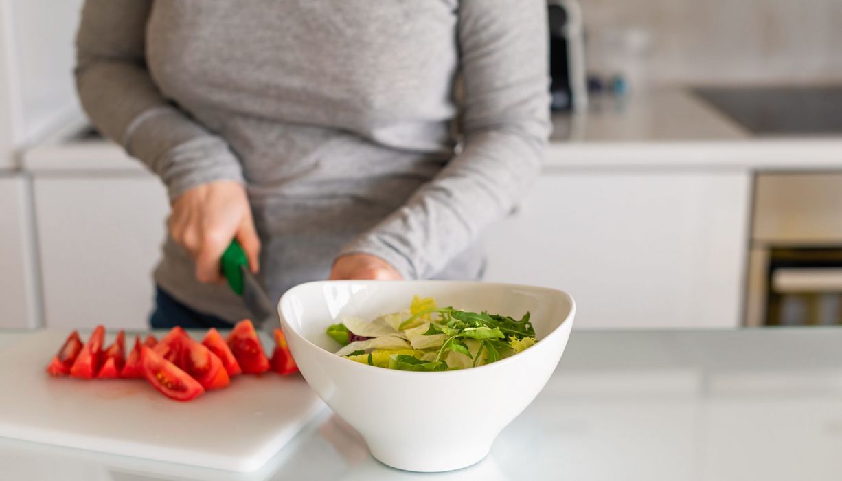 Frau, schneidet Tomaten und macht sich einen Salat.